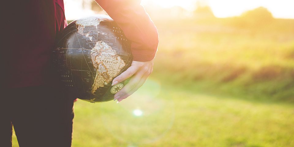 [Translate to English:] Person auf Wiese mit Globus in der Hand